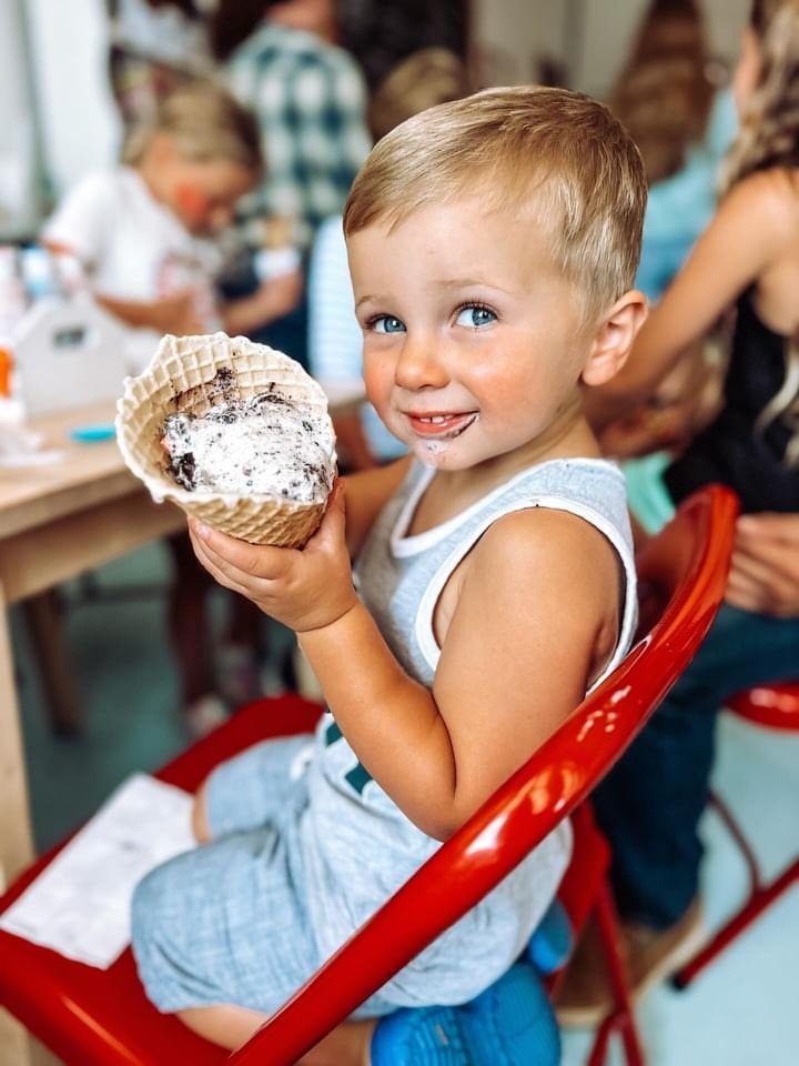 A smiling child enjoying ice cream in a house-made waffle cone at The Cherry on Top